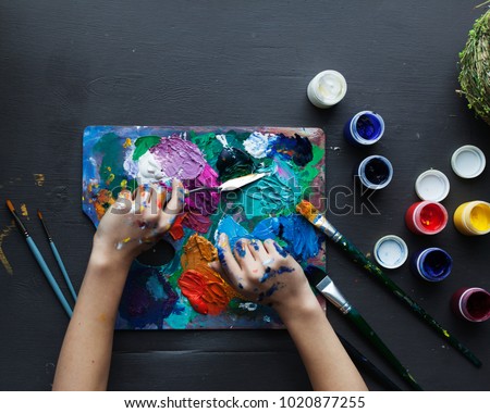 The artist's hands, paint palette brushes, different colors. The girl is drawing. The artist's tools for real art and inspiration. Dark light. Top View.