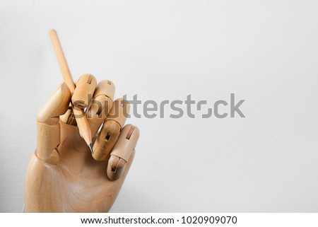 High resolution closeup of art model wooden hand holding a wooden pencil isolated on textured white paper, Flash light made smooth lighting on wooden hand and smooth shadow on textured white paper.