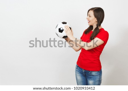 Smiling European young woman, two fun pony tails, football fan or player in red uniform hold classic soccer ball isolated on white background. Sport play football healthy lifestyle concept. Side view
