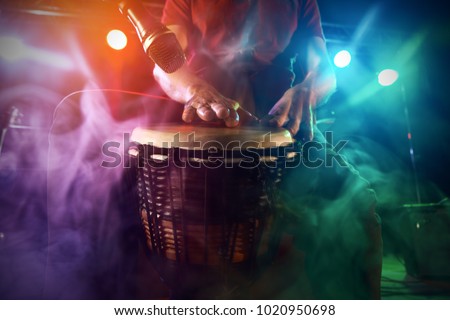 The musician plays the bongo on stage. Stage light. Smoke.
