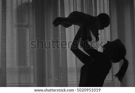 Silhouette of young mother holding her baby in her hands. Black and white picture.