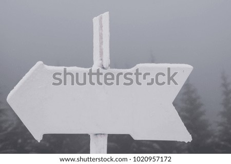 Arrow shaped metal outdoors sign covered in snow