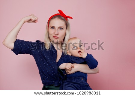 Yes, you can. Young beautiful blonde mother with a cute baby. Conceptual gesture to show the biceps Royalty-Free Stock Photo #1020986011