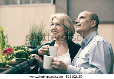 Smiling couple of pensioners drinking tea and chatting on balcony
