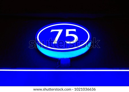 The glowing blue light of the number 75 indicates the number of the house in the dark