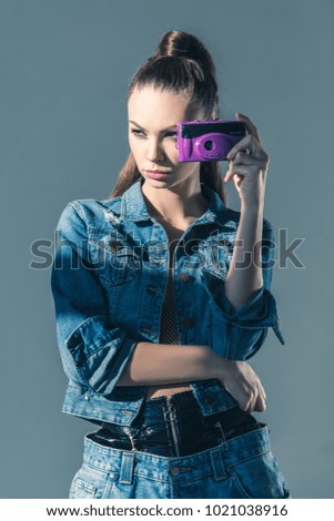 brunette girl posing in denim clothes with retro camera, isolated on grey