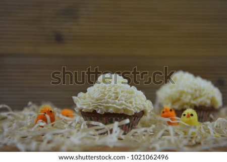rustic Easter time of vanilla and butter cream cupcakes surrounded with decorations of straw with yellow and orange color small chicks