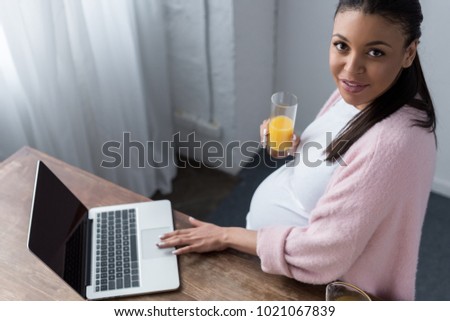 african american pregnant woman with orange juice using laptop
