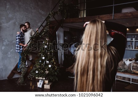 Photographer girl with long blondie hair take picture of a young romantic couple in love at cozy home