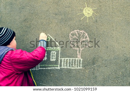 The boy draws a house on the wall.