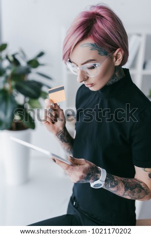young tattooed businesswoman holding credit card and using