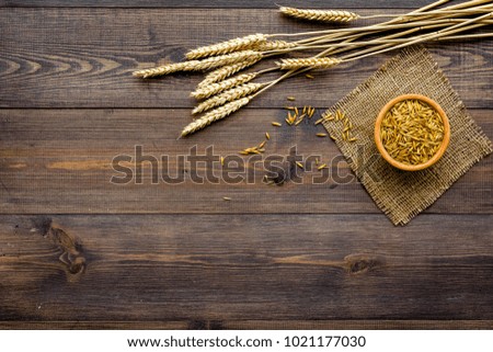 Raw oats in bowl near sprigs of wheat on dark wooden background top view copy space