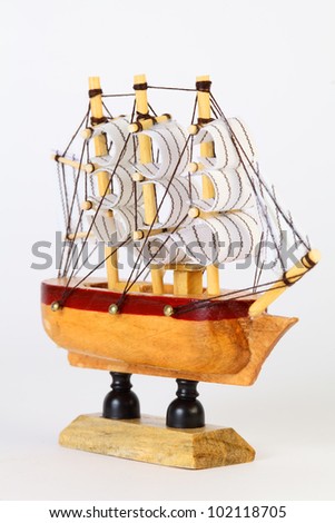 Small wooden model of sailing ship with rigging and white sails on stand