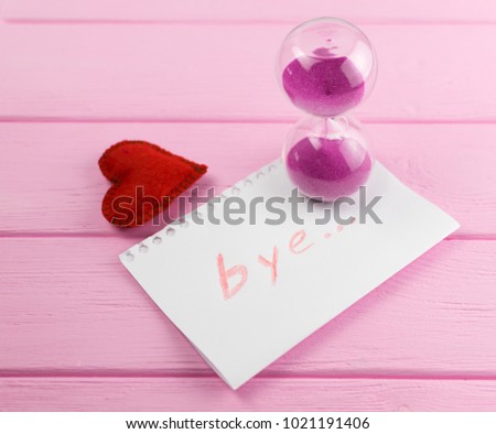 End of love. Hourglass and the word "bye" on a piece of paper with a heart next to it.