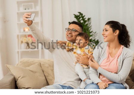 family, technology, parenthood and people concept - happy mother and father with baby daughter taking selfie by smartphone at home