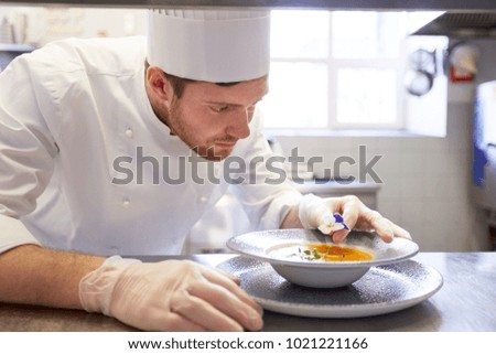 food cooking, profession and people concept - happy male chef cook serving and decorating plate of soup with flower at restaurant kitchen