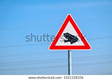 Frogs crossing the road warning sign against blue sky