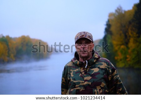 Portrait of an old man in military uniform sternly looks at the camera. Early morning fog and rain