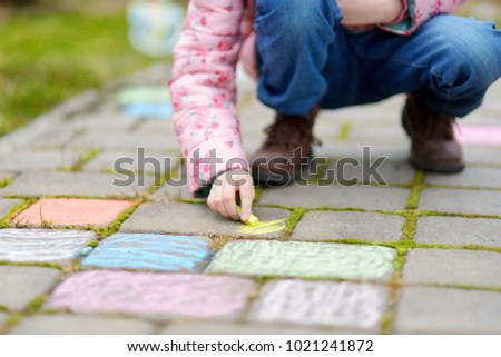 Close-up on little girl's hand drawing with colorful chalks on a sidewalk. Summer activity for small kids. Creative leisure for family.