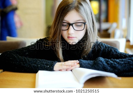 Adorable school aged kid girl in glasses reading book indoor. Education and reading