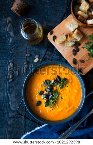 
Pumpkin soup in a bowl served with croutons, olive oil and pumpkin seeds. Dark wooden background.Flat lay food.