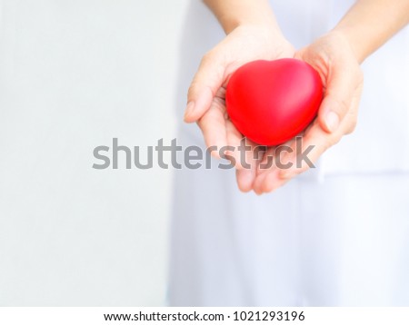 Selective focus of red heart held by female nurse's hands, representing giving all effort to deliver high quality service mind to patient. Professional, Specialist in white uniform isolated on white