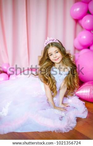 Girl with blond long hair in light-pink dress of a princess and tiara with pink balloons around

