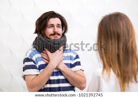 Bearded caucasian ill teenager with gray scarf around the neck visits the doctor