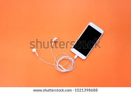 Smartphone and Earphones with Spiral Cable on Orange Background Top View Royalty-Free Stock Photo #1021398688