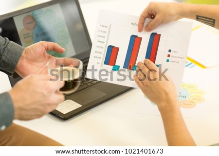 Cropped close up of two businessmen examining colorful graphics and diagrams working at the office laptop on the background team teamwork partnership development analysis strategy planning.