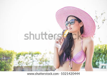 Beautiful asian female model drinking cocktail holding hand glass posing by the pool, outdoor portrait banner. Beach asian woman having fun in summer vacation holidays. Girl in tropical summer weather