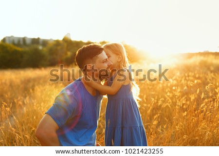 Family time. Father and daughter on the meadow at sunset. The little girl kisses her father on the cheek. Back light. Leisure together.