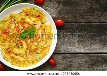 Omelet (omelette, Scrambled) with green onion, tomato on wood table. Easy to cook. Put some soy sauce, sugar and pepper. Famous in Thailand. Still life food. Vegetarian. Copy space. Royalty-Free Stock Photo #1021430656