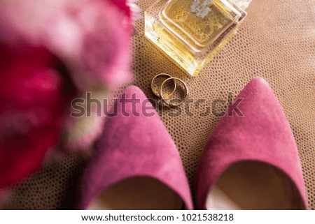 Golden wedding rings in focus on brown background with bridal shoes, perfume and flowers out of focus.