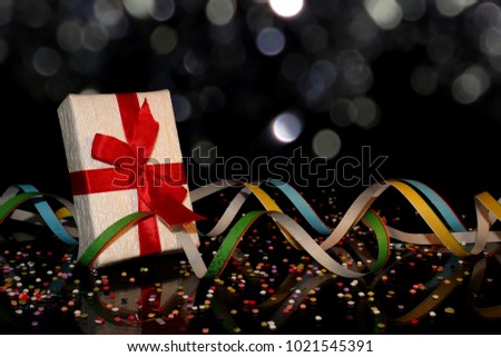 beautiful gift with red ribbon on black background with multicolored confetti