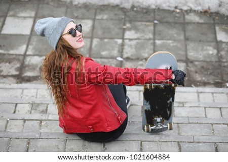 A young hipster girl is riding a skateboard. Girls girlfriends for a walk in city with a skateboard. Spring sports on the street with a skateboard.
