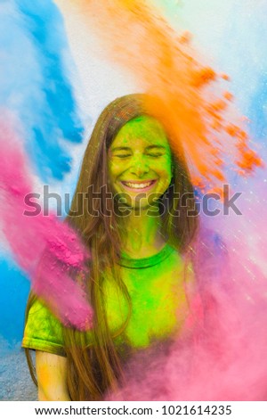 Holi festival. Young cheerful girl under explosion of colored powder at Holi colors (paints) party. Freeze motion (stop motion) of color powder exploding or throwing colour powder. Glitter explosion. Royalty-Free Stock Photo #1021614235