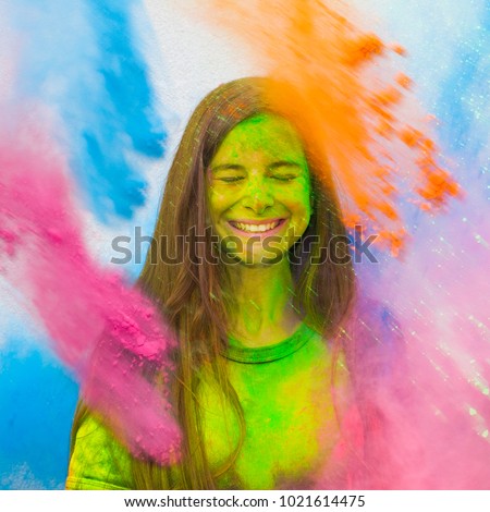 Happy holi. Young cheerful girl under explosion of colored powder at Holi colors (paints) party. Freeze motion (stop motion) of color powder exploding or throwing colour powder. Glitter explosion. Royalty-Free Stock Photo #1021614475
