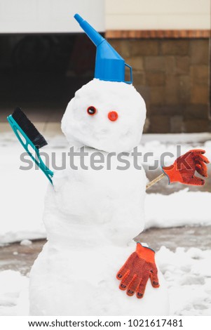 Snowman motorist stands in front of the garage. For decoration use a watering can, a brush and working gloves
