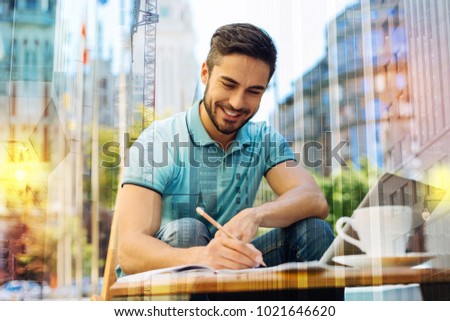 Young writer. Cheerful smart creative young author feeling excited and glad while sitting alone in a quiet place and smiling while writing the last chapter of his future book Royalty-Free Stock Photo #1021646620