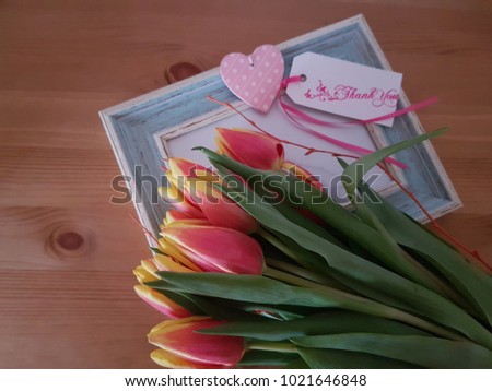 Tulips with a picture frame and thank you note laying on a wooden table