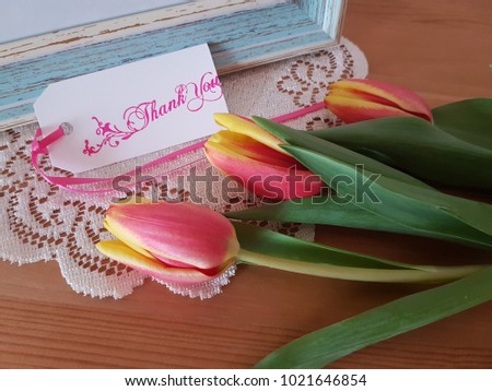 Tulips with a picture frame and thank you note laying on a wooden table