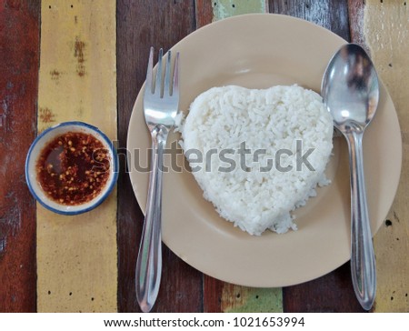 Steamed rice in a plate and chili paste on a wooden table.