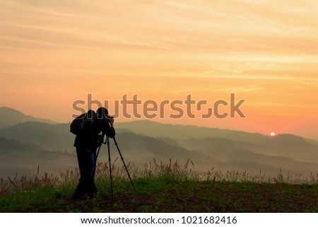 Photographer take photos with mirror camera on peak of mountain.  misty  landscape, spring orange pink misty sunrise in beautiful valley below.