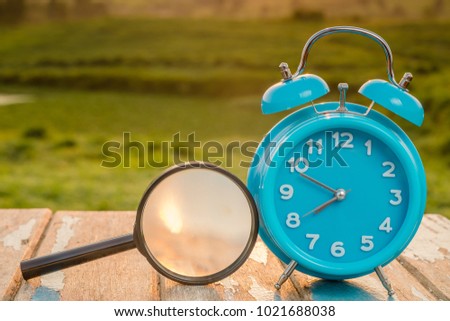 Alarm clock and magnifying glass standing on  wooden table against green background