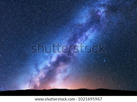 Milky Way. Fantastic night landscape with bright milky way, sky full of stars, yellow light and hills. Shiny stars. Beautiful scene with universe. Space background with starry sky. Astrophotography