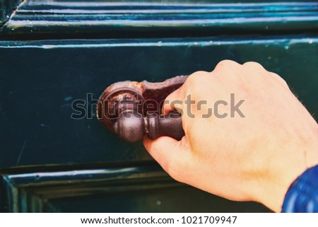 A man's hand opens the door, a close-up photo. The hand holds onto the antique metal handle of the green-blue door.