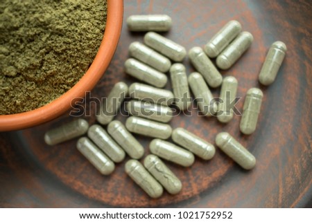 Supplement kratom green capsules and powder on brown plate. Herbal product alt-medicine kratom is  opioid. Home alternative pain remedy, opioid addiction, dangerous painkiller. Selective focus Royalty-Free Stock Photo #1021752952