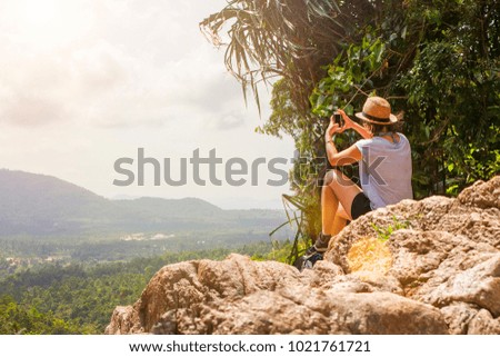 Travel for photos, life with a phone always concept. The girl woman traveler tourist hat sits high on the mountains rocks amazing view and make a photo on the mobile phone smartphone. 