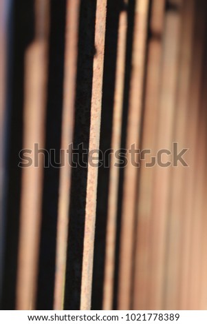Close up side view of rusty bars of an old mettalic gate. Pattern composed with vertical brown and dark lines. Iron aligned elements lighted by the sun. Blur background with shadows. Abstract picture.